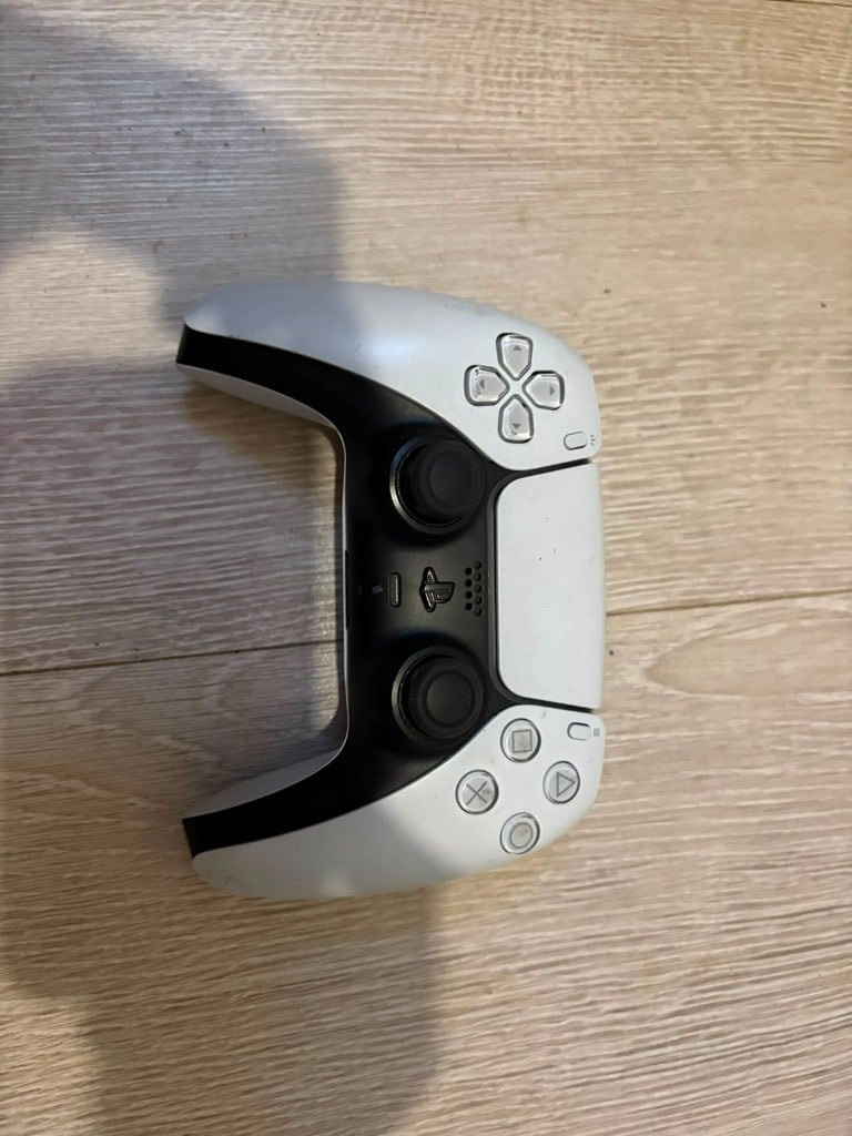 White and black DualSense controller on a wooden floor
